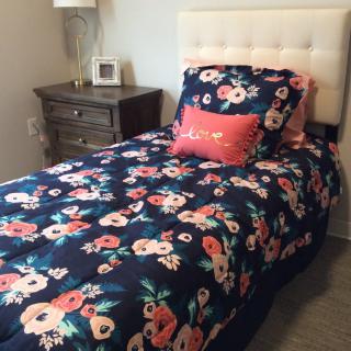 A cozy bedroom featuring a bed with floral bedding and decorative pillows next to a nightstand and lamp.