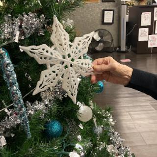 A beautifully crafted snowflake ornament being placed on a festive Christmas tree.