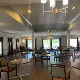 A spacious dining room with neatly arranged tables and chairs, featuring natural light streaming through large windows.