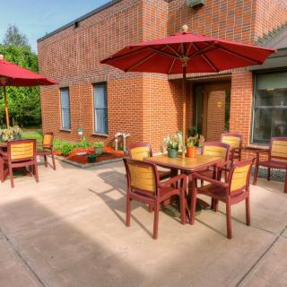 A cozy outdoor patio area with tables, chairs, and red umbrellas next to a brick building.
