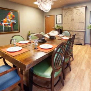 A cozy dining room with a wooden table set for a meal, surrounded by colorful chairs and decorated with modern artwork.