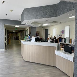 A hospital reception area with a front desk and office equipment, leading to a corridor.