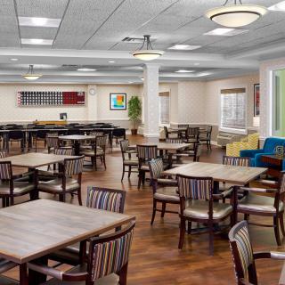 An empty dining area with neatly arranged tables and chairs, featuring wooden flooring and elegant chandeliers.