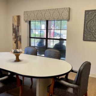 A conference room featuring a large oval meeting table surrounded by chairs, with artwork on the walls and a window offering a view outside.