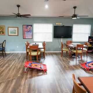 A spacious room with multiple tables and chairs, decorated with artwork on the walls and featuring wooden flooring.