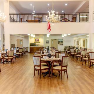 A spacious dining area with elegant chandeliers, wooden floors, and neatly arranged tables and chairs.