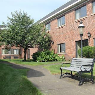 A serene outdoor area featuring a brick building, a park bench, and well-maintained greenery.