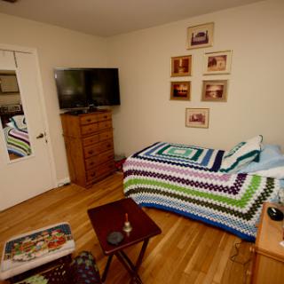 A cozy bedroom featuring a colorful crochet blanket on the bed, a TV mounted on the wall, and decorative photographs hanging above.