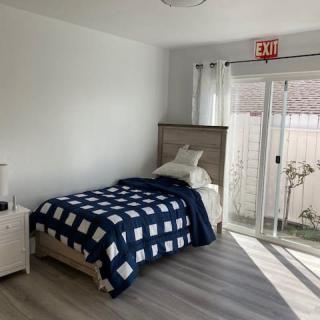 A minimalist bedroom with a single bed and a large sliding glass door allowing natural light to fill the room.