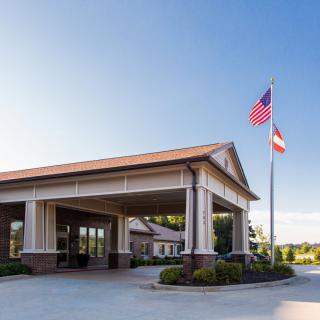A building entrance with two flags, surrounded by neatly trimmed landscaping under a clear blue sky.