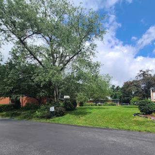 A scenic view of a grassy area with a large tree under a partly cloudy sky.