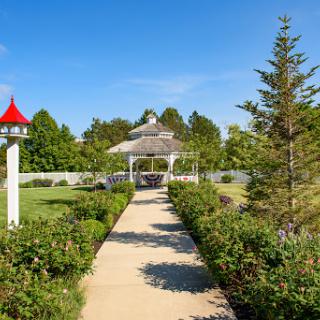 A picturesque garden pathway leading to a charming gazebo under a clear blue sky.