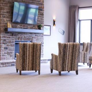 A modern living room with striped chairs facing a mounted TV above a brick fireplace.