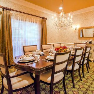 An elegantly decorated dining room featuring a large dining table with chairs, set under a sparkling chandelier.