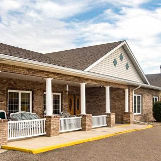 A brick building with a front porch and white columns under a partly cloudy sky.