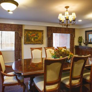 A stylish dining room featuring a wooden table with elegant chairs, adorned with a chandelier and decorative artwork.