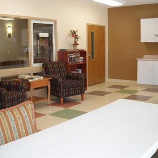A spacious waiting room featuring comfortable chairs and a kitchenette, designed with colorful floor tiles.