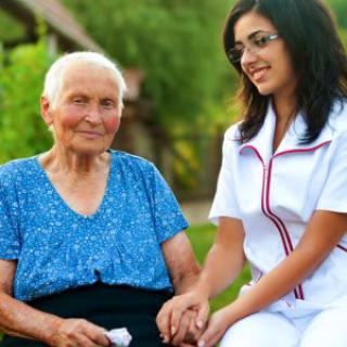A caregiver provides support to an elderly woman in a peaceful outdoor setting.