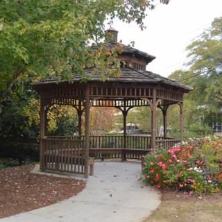 A wooden gazebo surrounded by trees and flowers in a park.