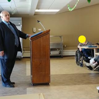 A speaker stands at a podium addressing an audience in a community setting.