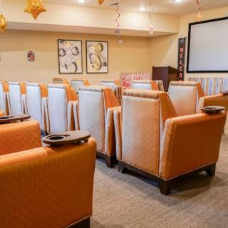 A cozy theater room with orange upholstered chairs facing a large screen.