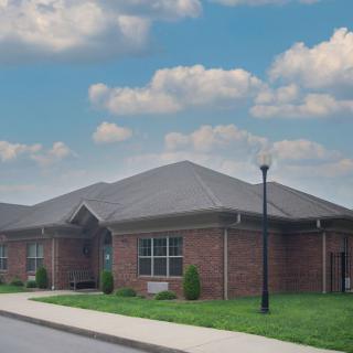 A brick building with a sloped roof, adjacent to a sidewalk and surrounded by grass under a cloudy sky.