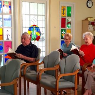 A group of seniors sitting indoors, engaging in a reading activity together.