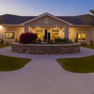A well-lit house exterior at dusk with a circular driveway and landscaping.