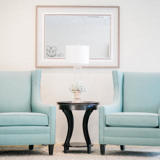 A minimalist living room setup with two blue chairs, a small round table, and a white lamp between them.