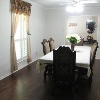 A well-furnished dining room with a table set for six, adorned with a floral centerpiece and elegant curtains.