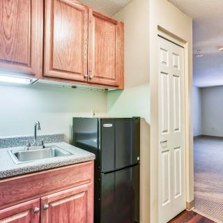 A compact kitchen area with wooden cabinets, a sink, and a small refrigerator in an apartment setting.