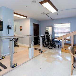 A rehabilitation room equipped with parallel bars, a wheelchair, and a ramp for physical therapy exercises.