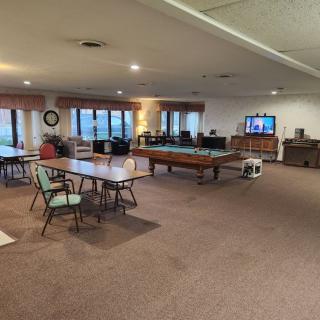 A spacious game room featuring a pool table, several tables and chairs, a television, and large windows.