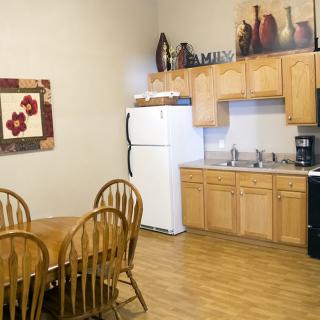 A cozy kitchen with wooden furniture and decor, featuring a dining table, chairs, refrigerator, oven, and cabinets.