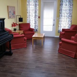 A cozy living room featuring a piano, red upholstered chairs, and wooden flooring.