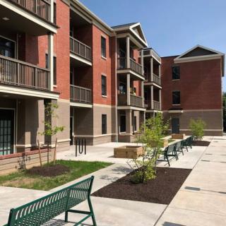 A modern apartment complex with a brick facade, featuring balconies and well-maintained outdoor spaces with benches and landscaping.