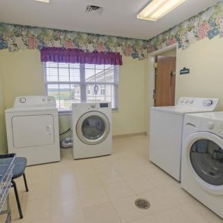 A laundry room with multiple washing machines and a dryer, featuring floral wallpaper and a window for natural light.