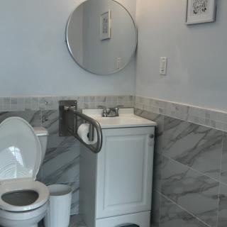 A modern bathroom featuring a toilet, sink, and round mirror with marble tile accents.