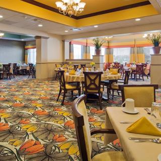 An elegantly designed dining room with multiple tables and chairs, featuring a colorful carpet and chandelier lighting.
