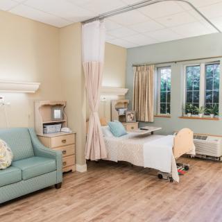 A tidy hospital room with a bed, sofa, and window.