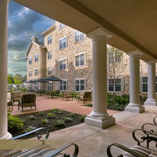A view of a courtyard with a stone building, featuring columns and outdoor seating.