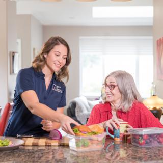 A caregiver assists a senior woman in preparing a healthy meal together.