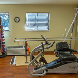 A rehabilitation therapy room equipped with a stationary bike, dumbbells, exercise balls, and parallel bars.