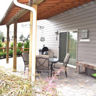 A cozy backyard patio with a table, chairs, and a barbecue grill under a wooden pergola.