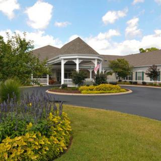 A building with a landscaped entrance and driveway under a partly cloudy sky.