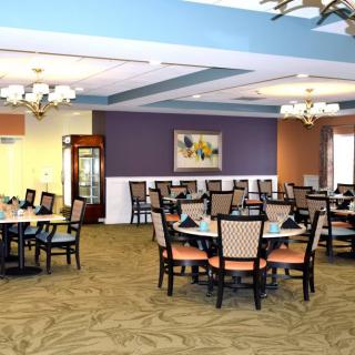 A spacious dining area with neatly arranged tables and chairs, elegant chandeliers, and a colorful wall painting.