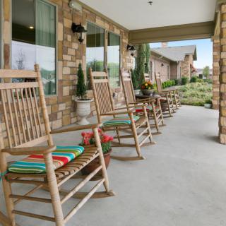 A row of wooden rocking chairs with colorful cushions on a brick porch.
