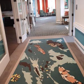A vibrant hallway featuring a decorative rug with colorful patterns, leading to a sitting area.