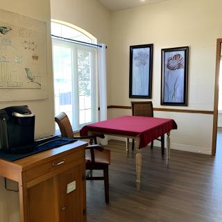 A cozy dining area with a table set for two, featuring artwork on the walls and a coffee machine nearby.