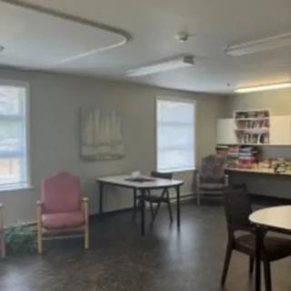 A room with tables, chairs, and a kitchenette setup.